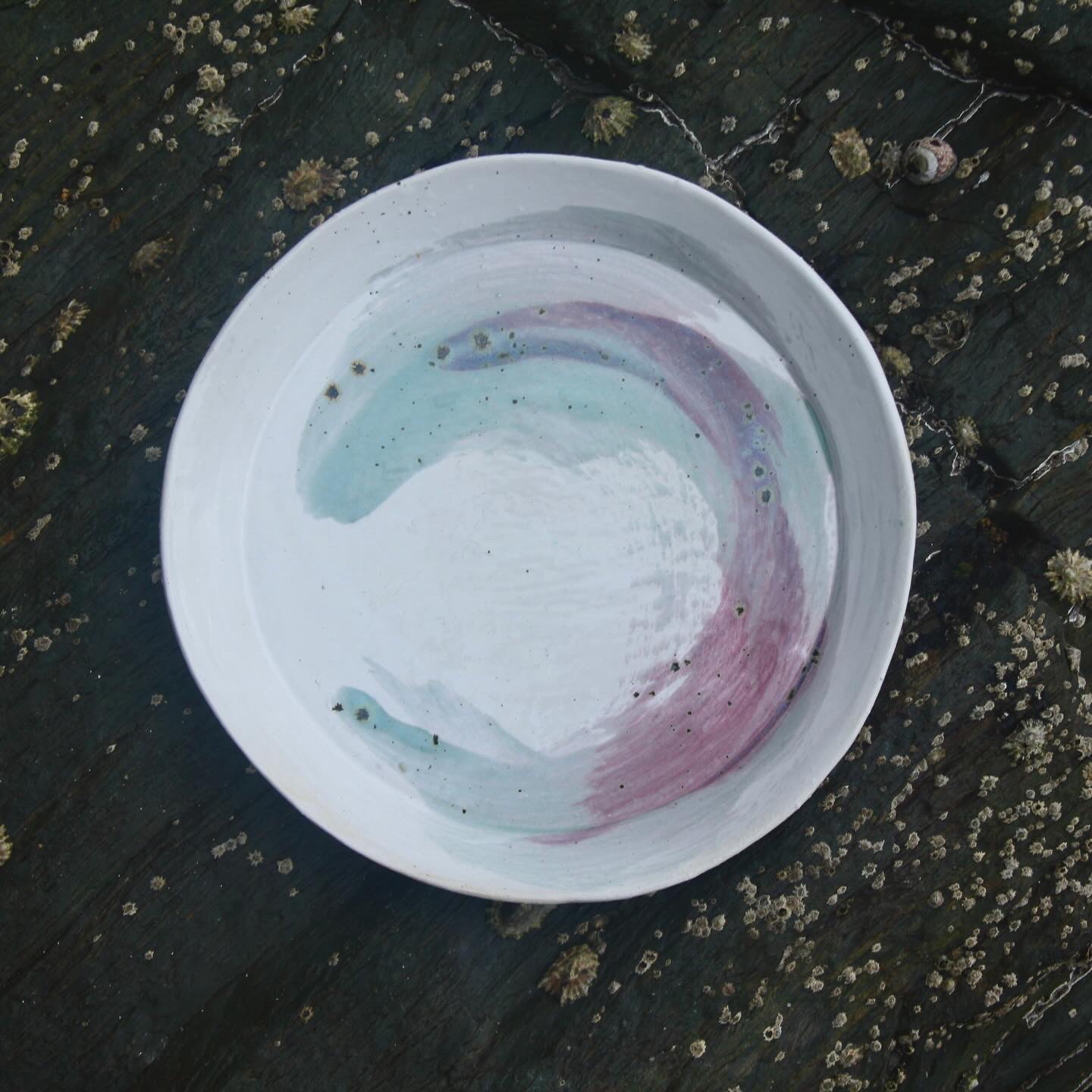 White plate with sweep of blue and pink gaze, sitting against dark black rock by the sea